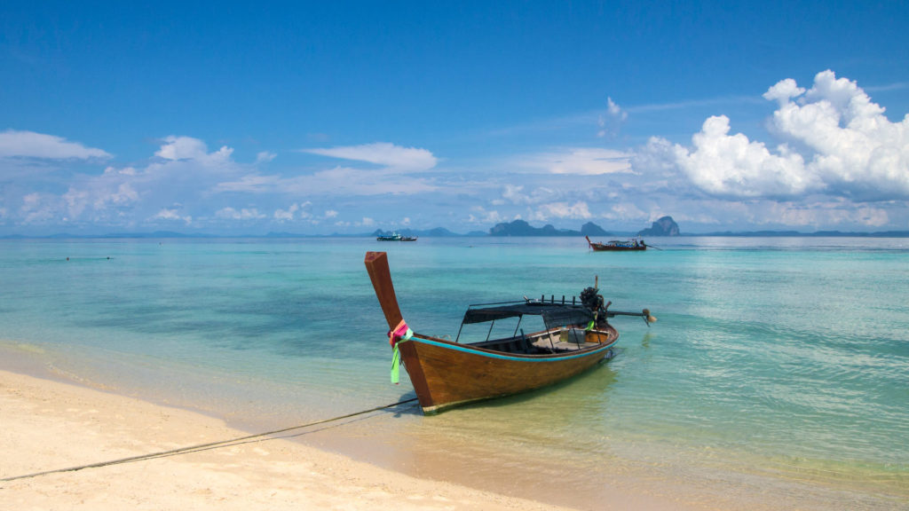Paradiesischer Strand auf Koh Ngai mit Aussicht auf Felsen und Longtail Boote